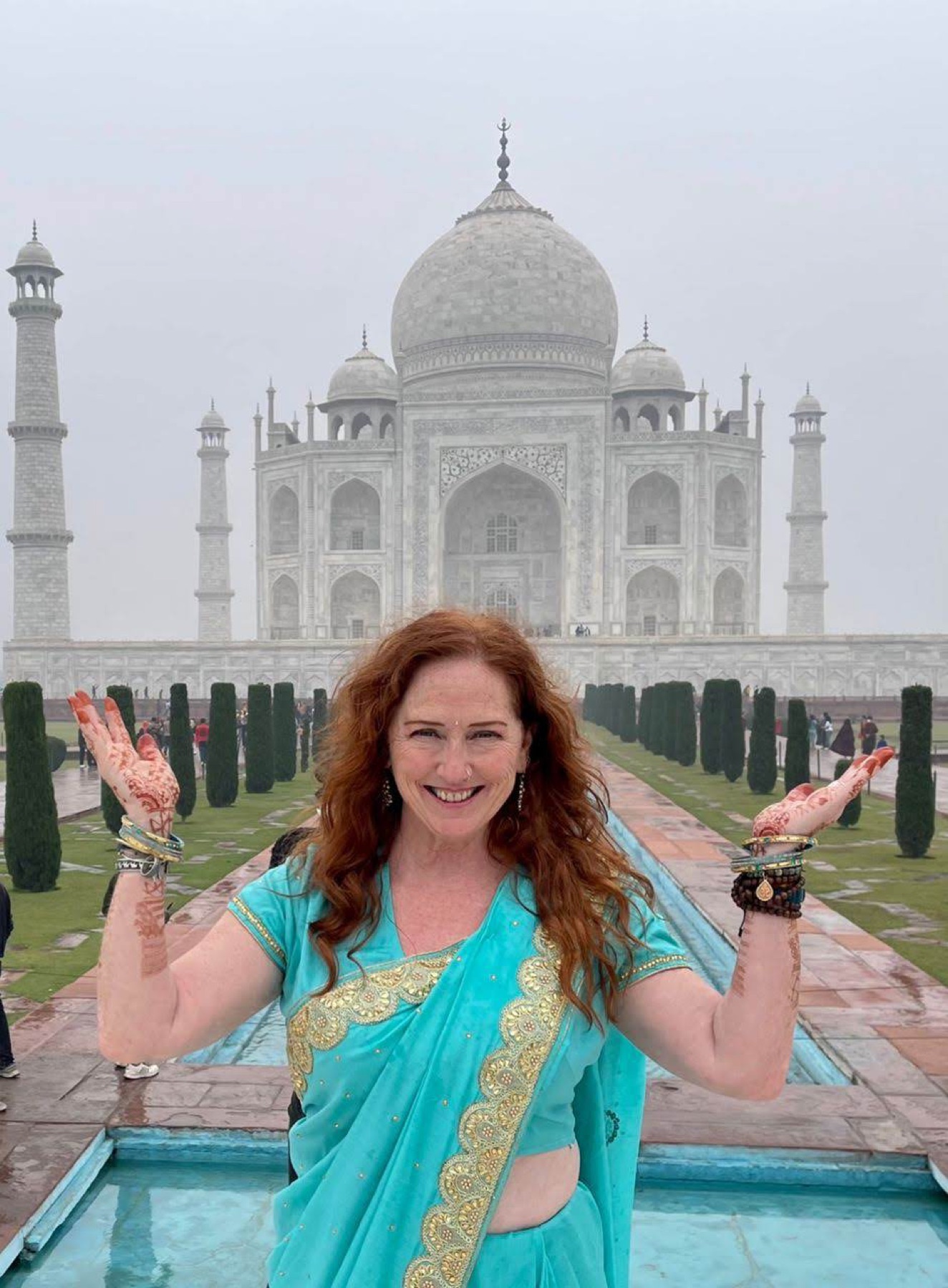 A guest in a turquoise sari, arms raised before the Taj Mahal